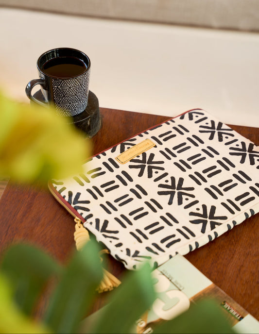 Stylish patterned laptop sleeve Nairobi – black and cream geometric design with tassel detail, lifestyle setup beside coffee cup from This Is Essential.