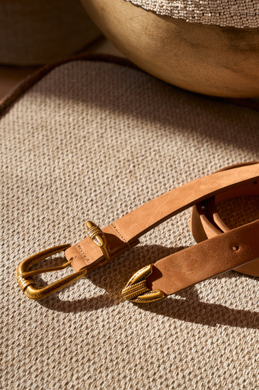 A tan Cairo buckle belt with a brass buckle placed on a textured surface.
