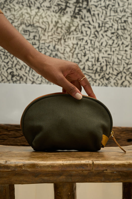 Hand holding a green canvas pouch on a wooden surface.