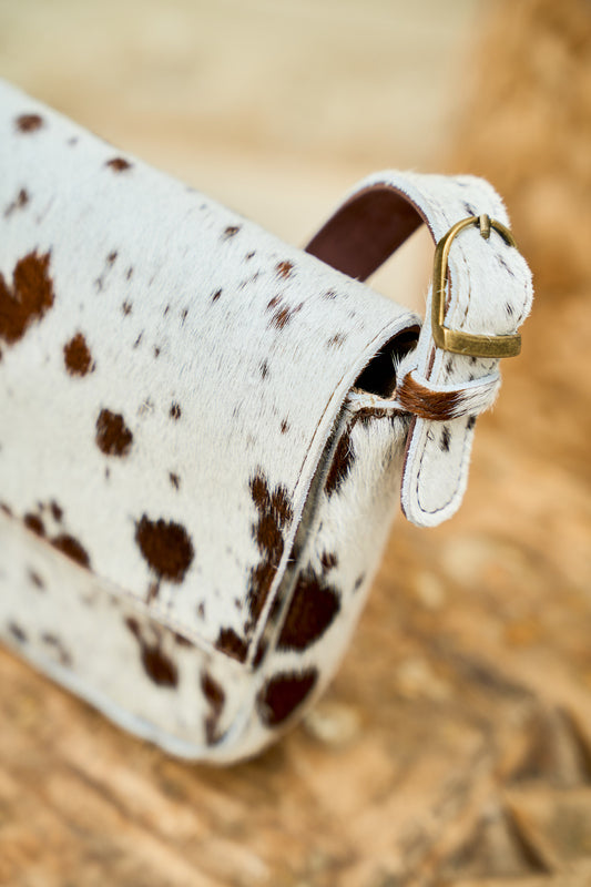 Close-up of a cow print handbag with a gold buckle strap for longer handle