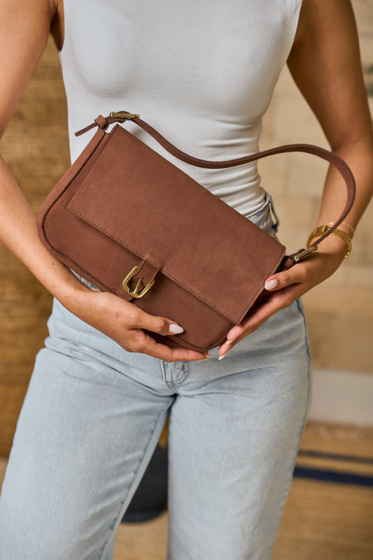 Person holding a brown suede leather handbag with a gold buckle