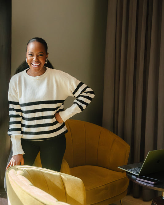 A woman wearing the classic striped knit sweater in a Cream and black color combination, paired with black pants.