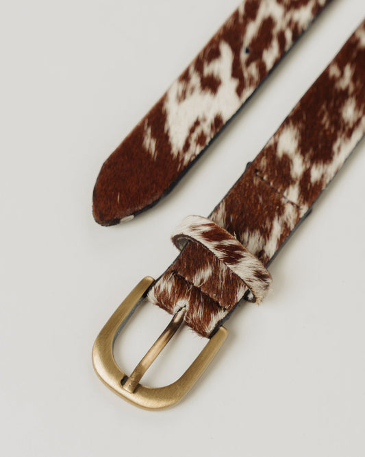 A cowhide belt with a brass buckle and brown and white strap, laid out flat.