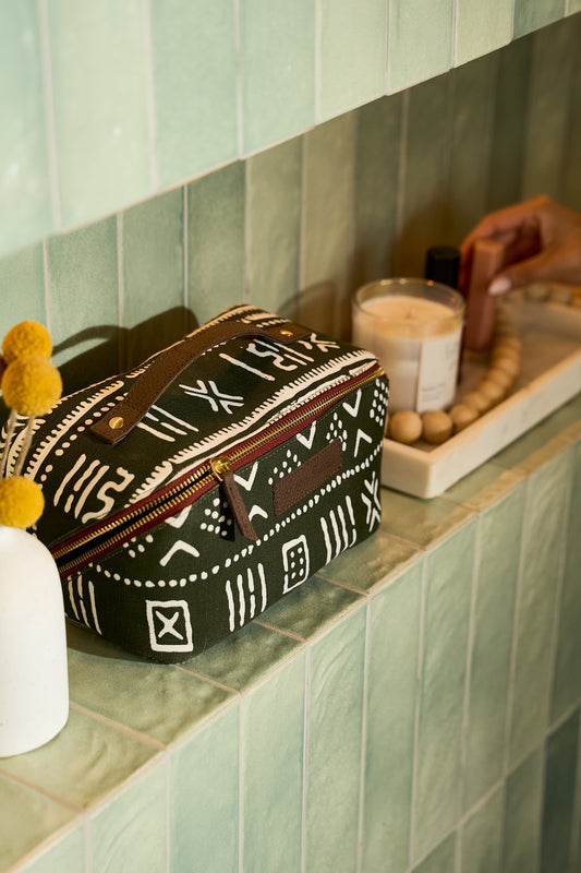 Zola toiletry bag in green/white mud cloth print canvas, featuring two spacious compartments, four interior pocket sleeves, waterproof navy lining, and genuine leather strap and zipper pull — a stylish, roomy organizer for skincare and makeup essentials.