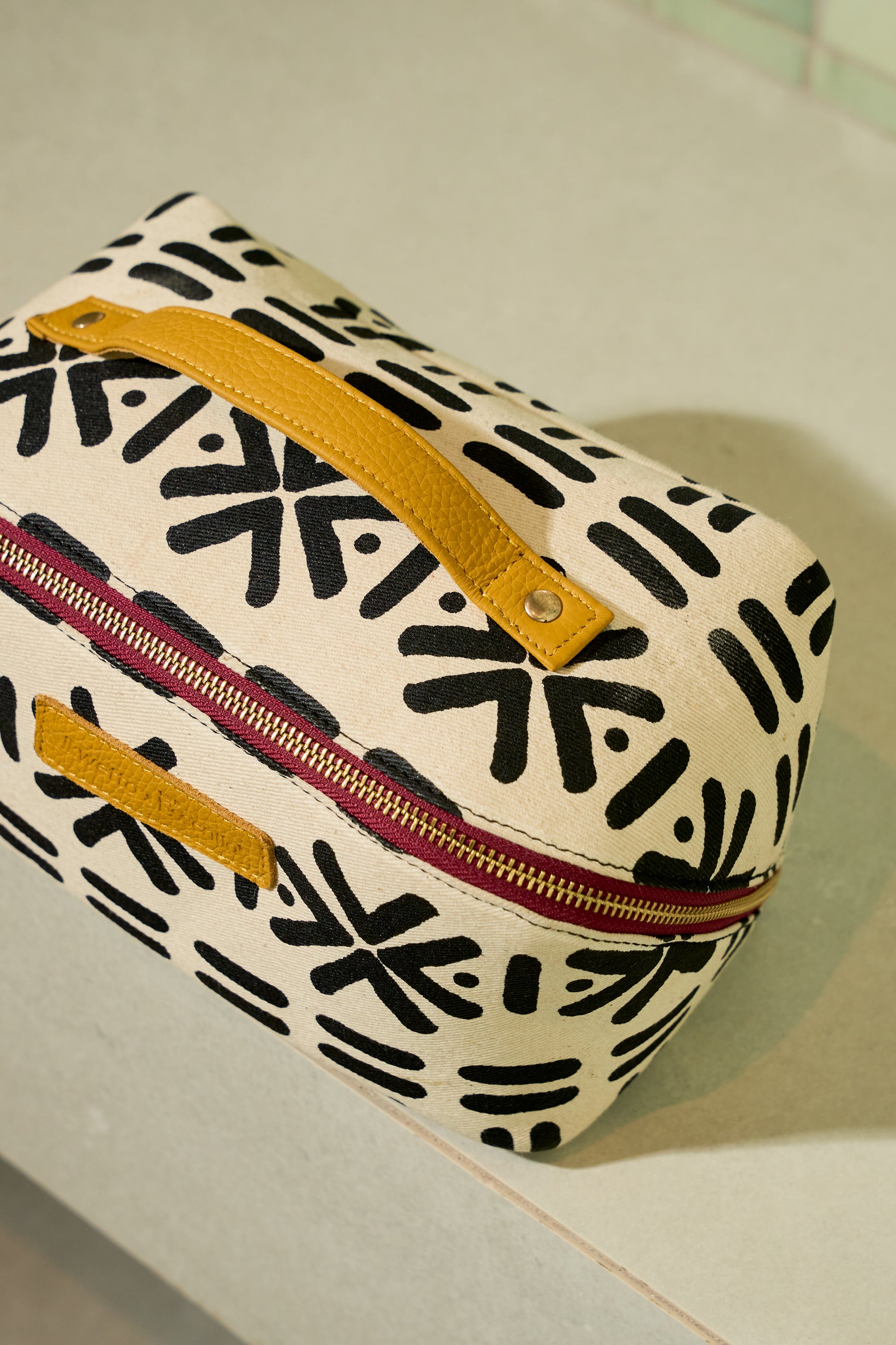 Toiletry bag in White mudcloth print with mustard leather handle.